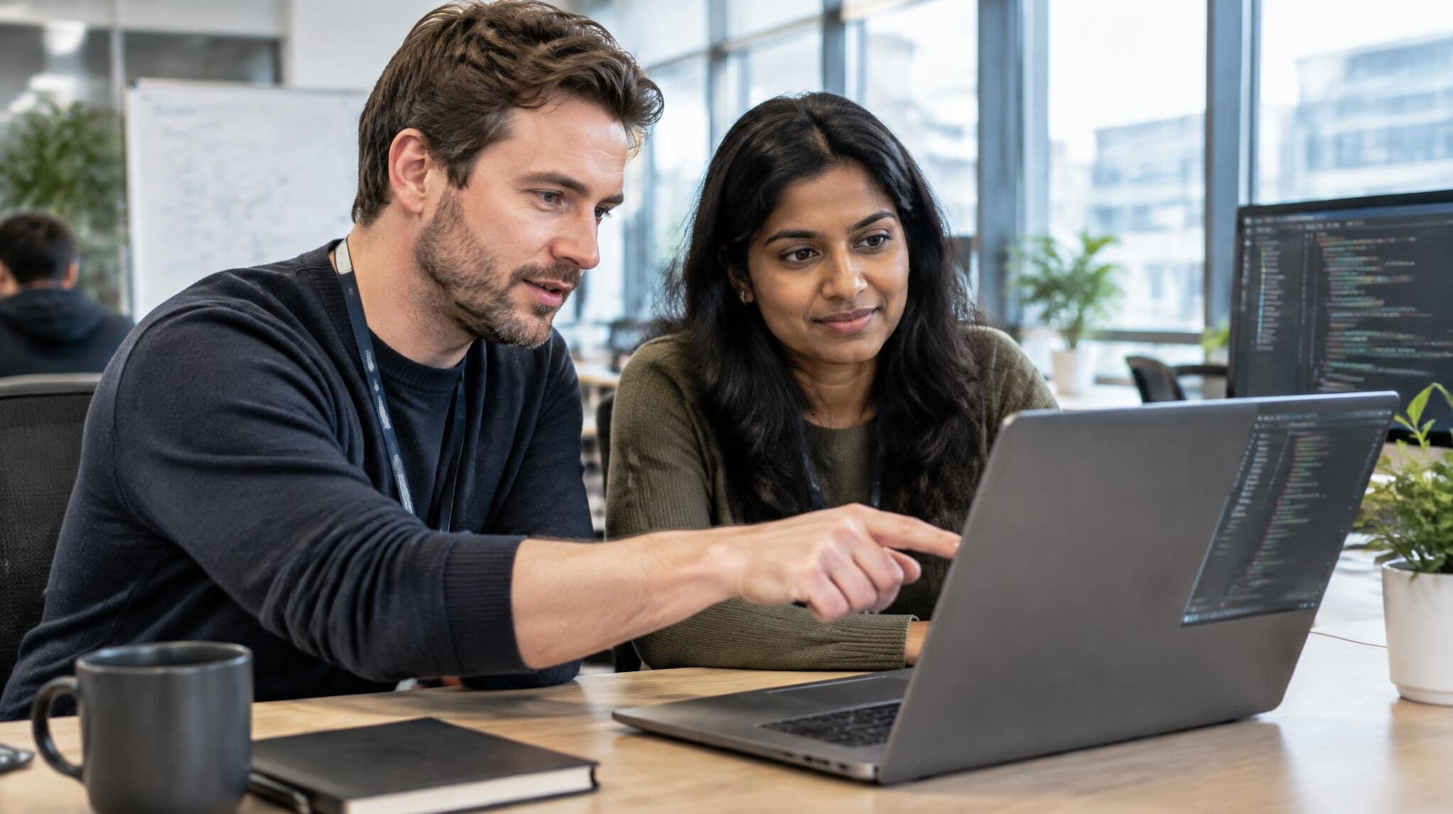Two developers reviewing code together on a laptop screen